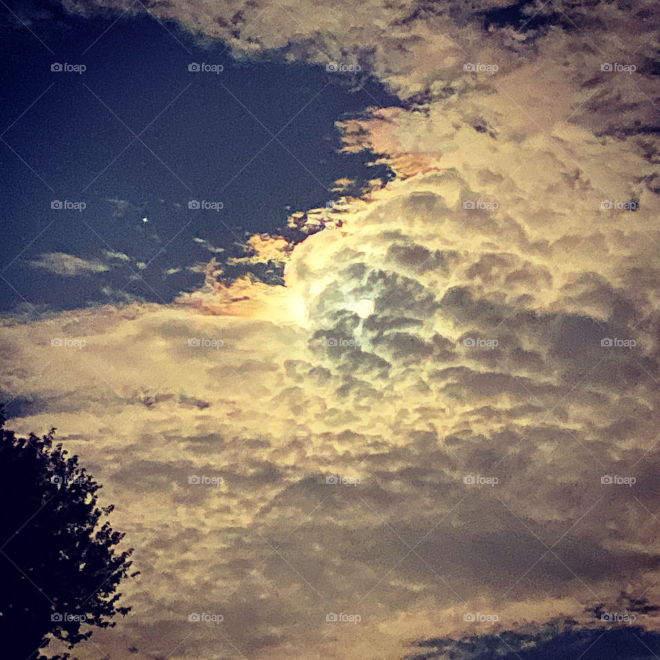 Moon hiding behind the clouds, middle of the night but a rich blue background and tinge of orange fill the sky.