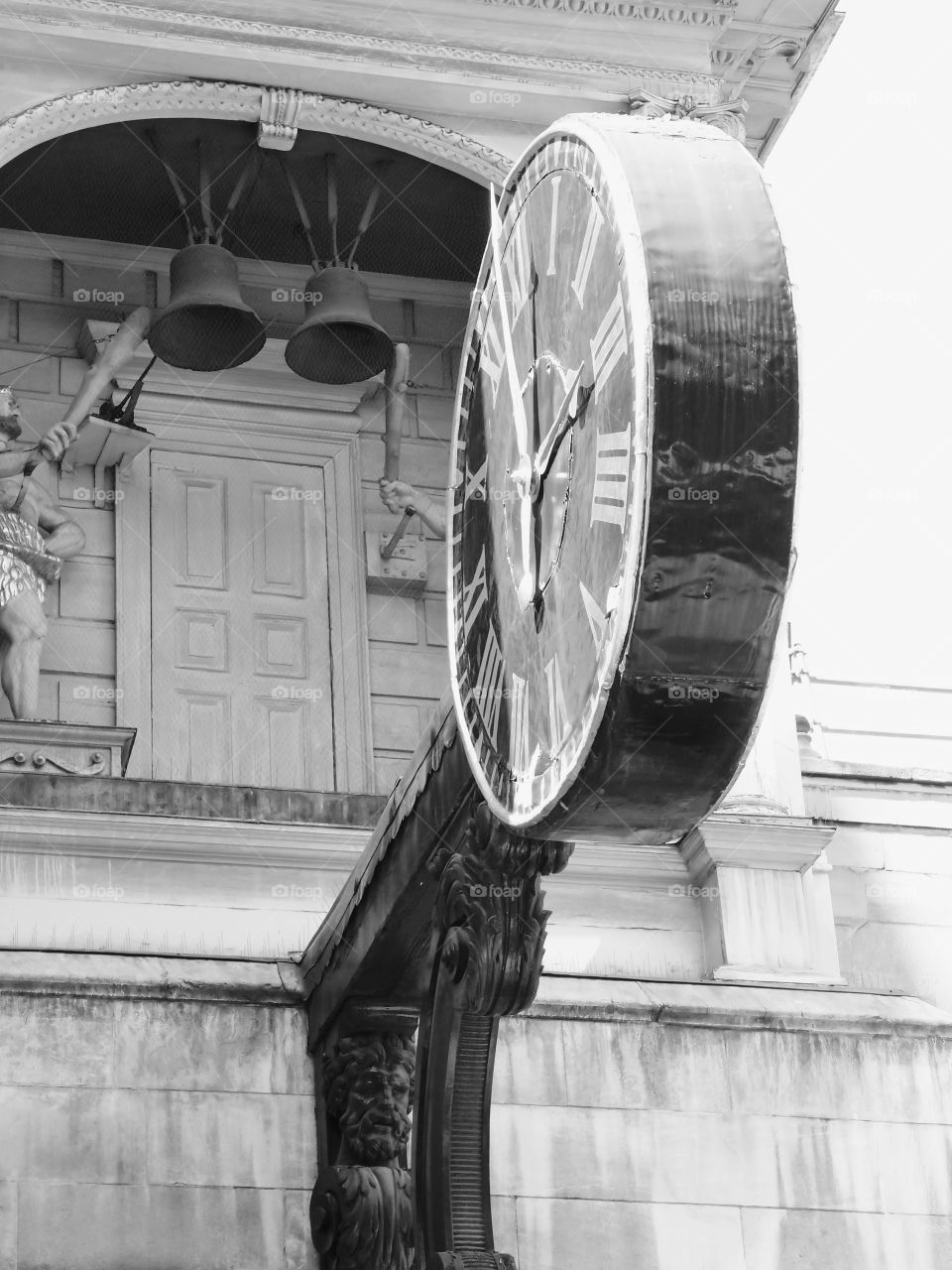 A large old clock mounted on a building of carved stone in Europe on a sunny summer day. 