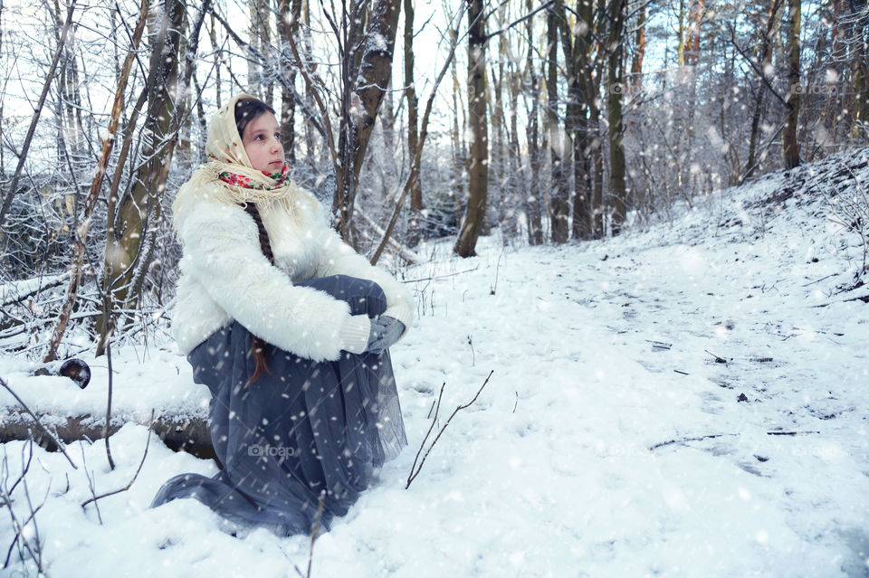 A girl in a scarf sits in a snowy forest