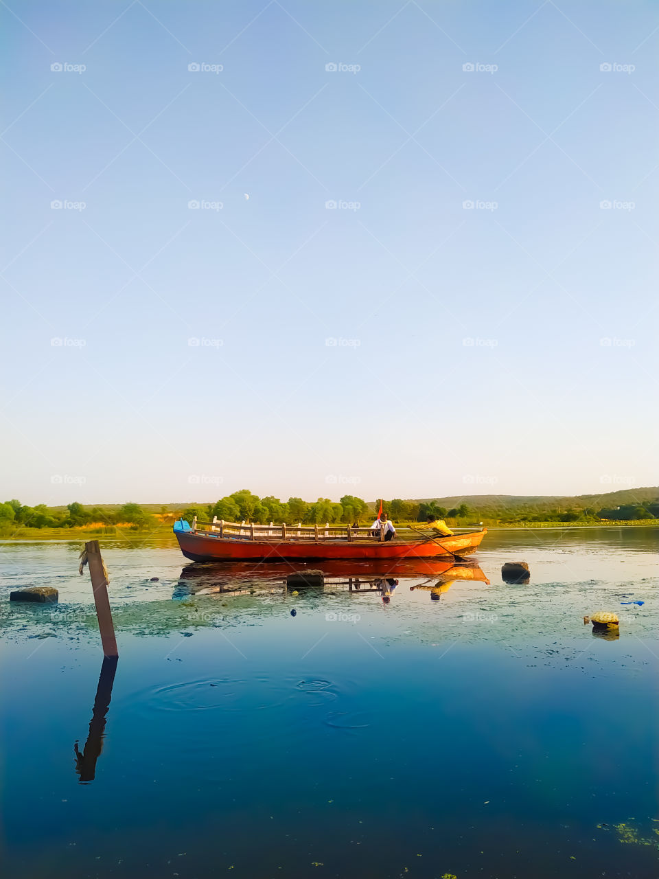 Two people roaming the river by boat together with green trees across the river
