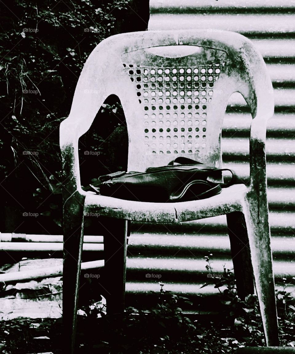 Behind the house where used goods are stored, there is a plastic chair that has been damaged and has not been used for a long time because it is considered an outdated chair
