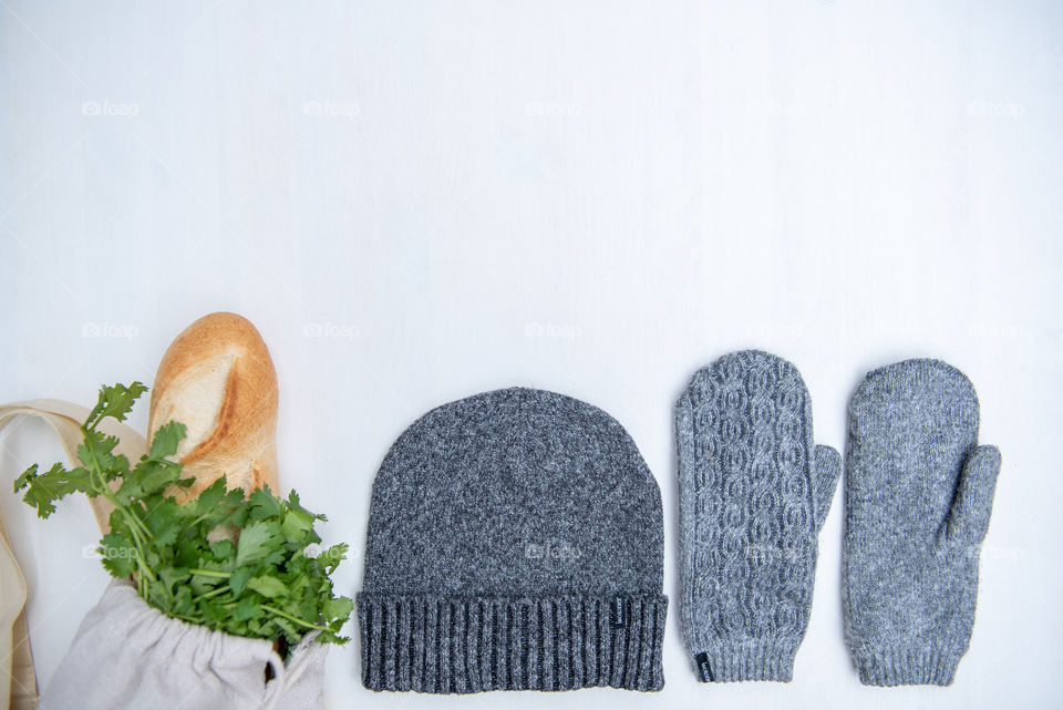 Flat lay of a knit beanie hat and mittens next to groceries in reusable grocery bags