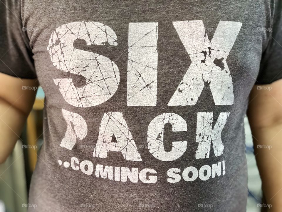 Man wearing shirt with word six pack coming soon for his inspiration that he want fo strong 