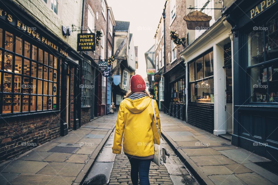 A fashionable young girl wearing a yellow coat and walking along The Shambles in York, UK which is a historic and medieval street with old fashioned buildings and shops