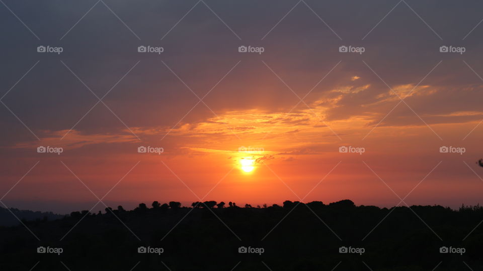 An orange sunset with yellow sun and grey clouds 