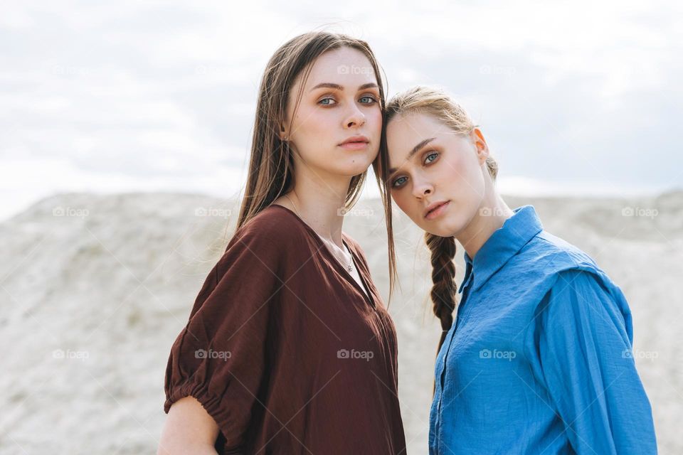 Fashion beauty portrait of young women sisters in brown and blue organic shirts on desert background