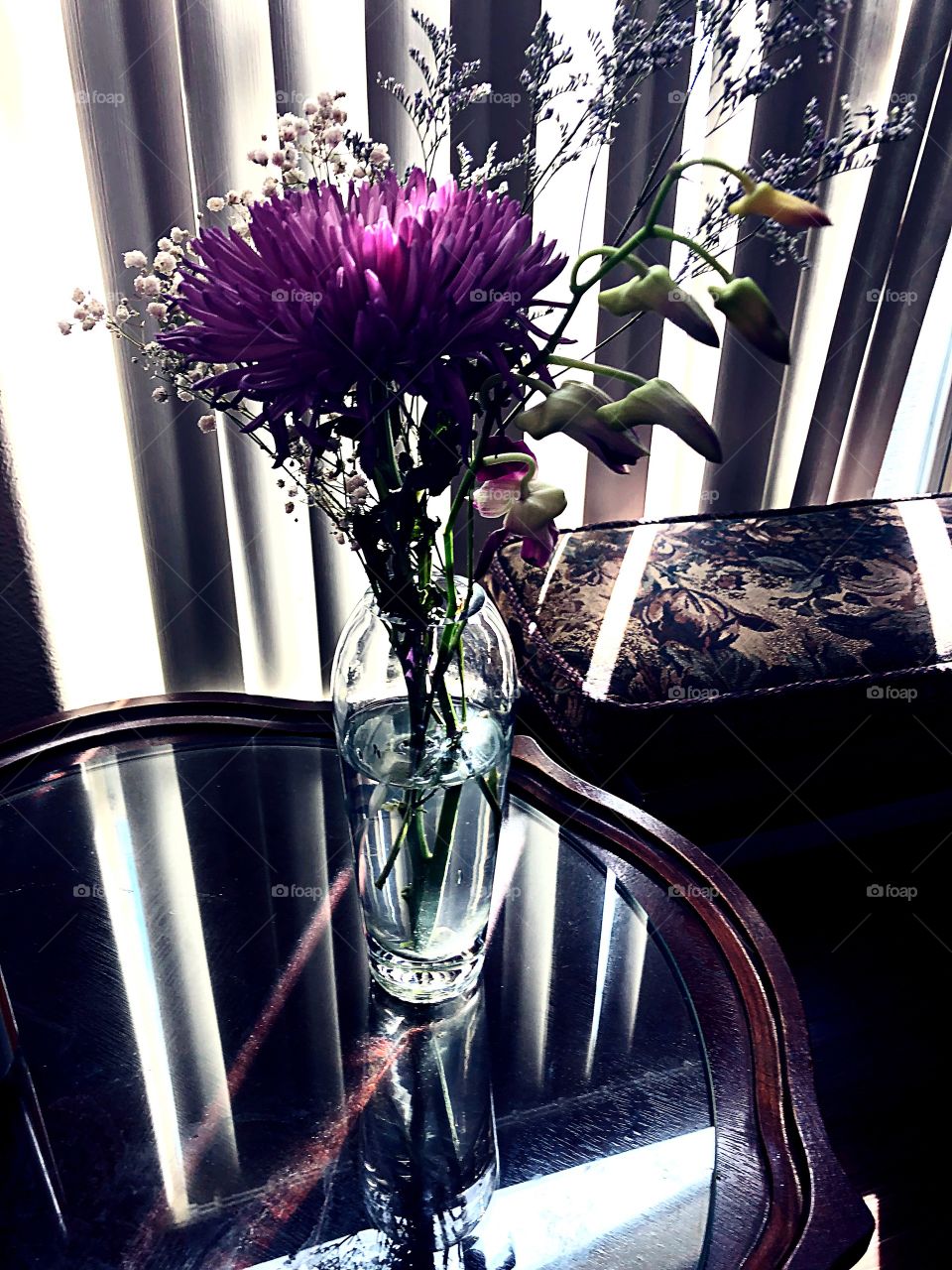 Flowers in a glass vase with light coming through blinds.