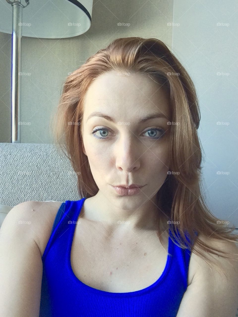 Big blue eyes, red hair, duck face pose selfie. Female model, long hair, tank top, lips pouted, sucked in cheeks.
