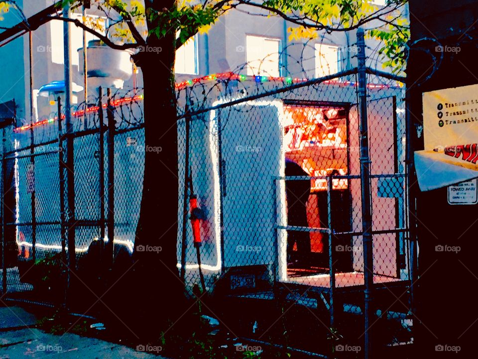 Behind the fence there is a food vendor setup for take-out only. It is located next to the parking lot underneath the Pulaski Bridge in Long Island City, Queens, New York. The photo was taken in the Spring of 2019. Hypnotic Productions