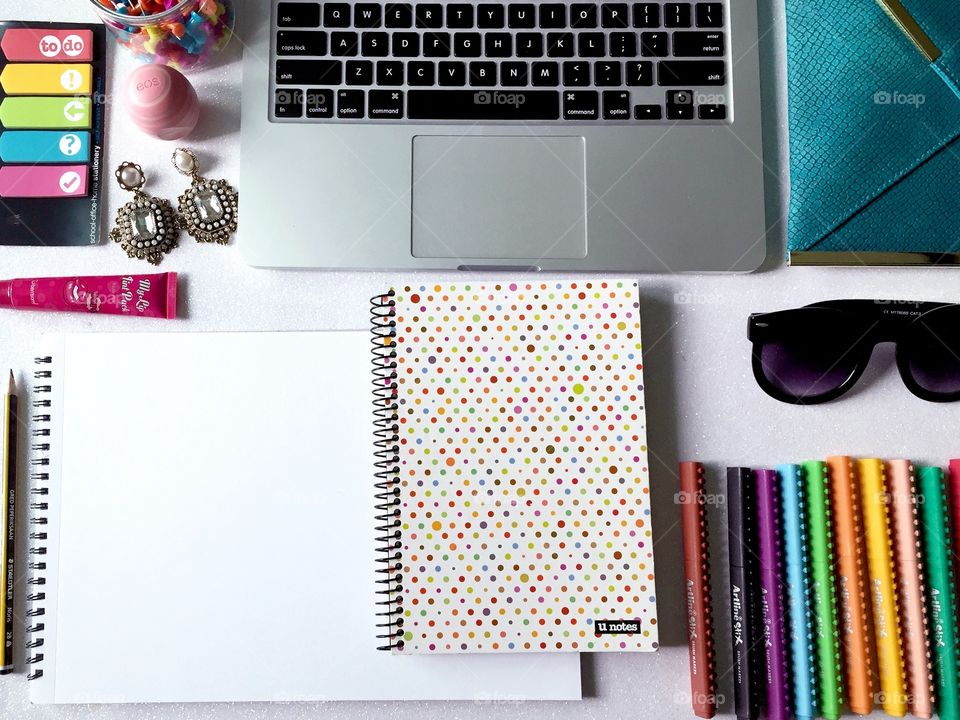 Top view of women's work desk with stationary, laptop, notebook, fashion accessories and empty sketch book.