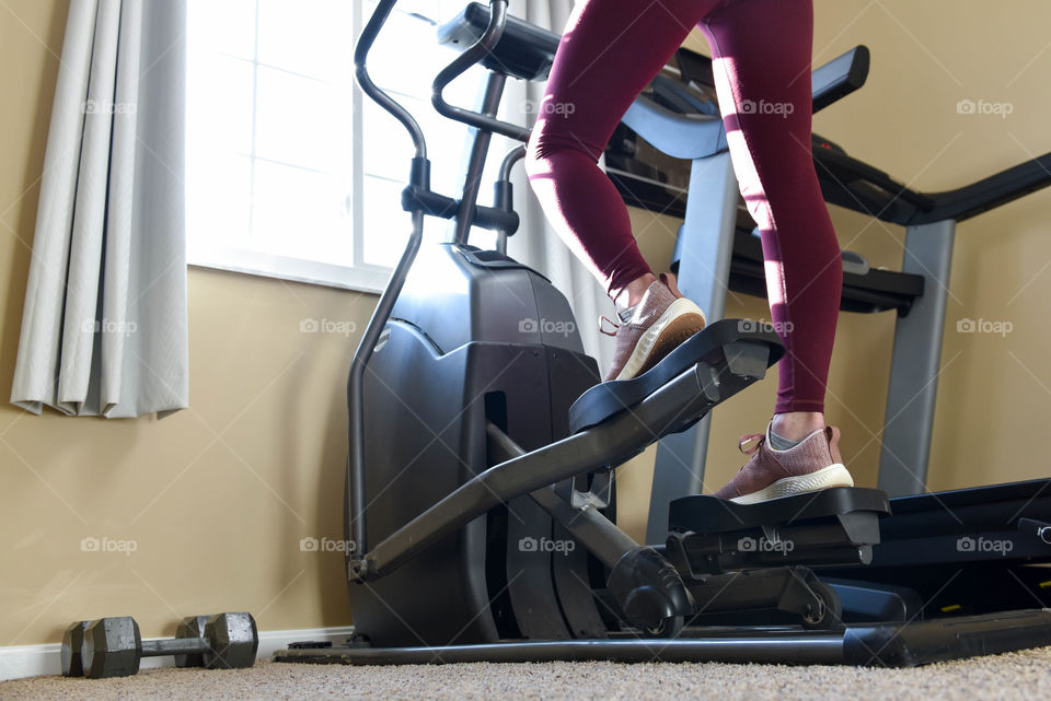 Close-up of a woman exercising on an elliptical machine indoors with sunlight coming through a window