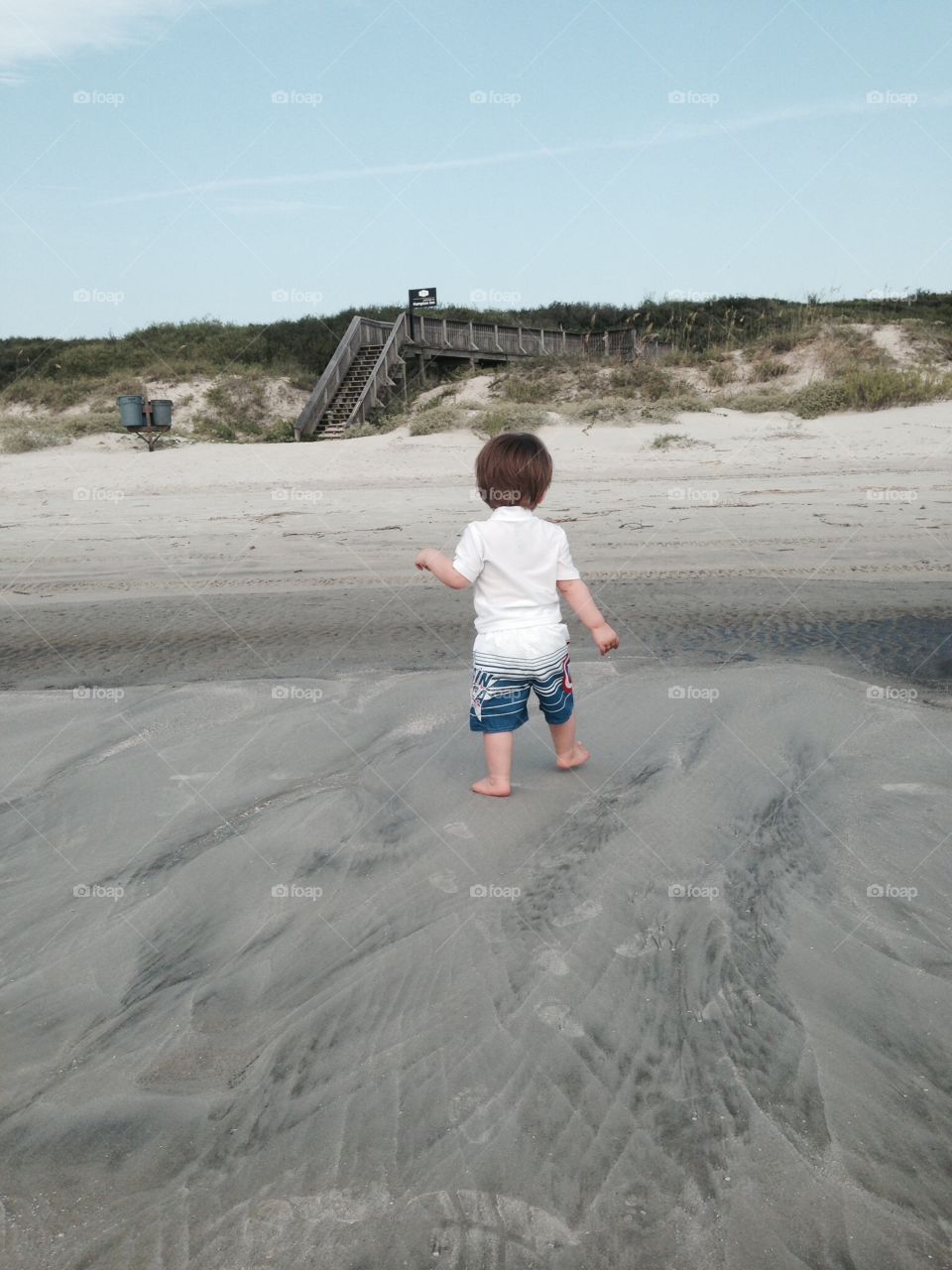 Toddler walking down the beach.
