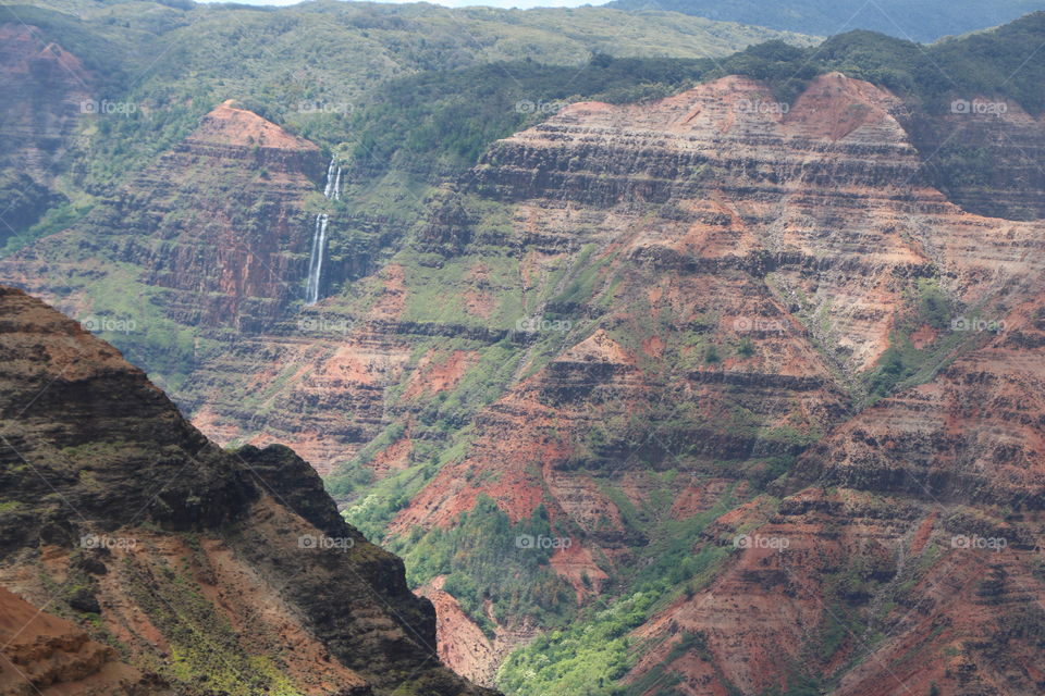Waimea Canyon on Kauai island , waterfall in a distance and green and earth coloured amazing scenery for the viewer