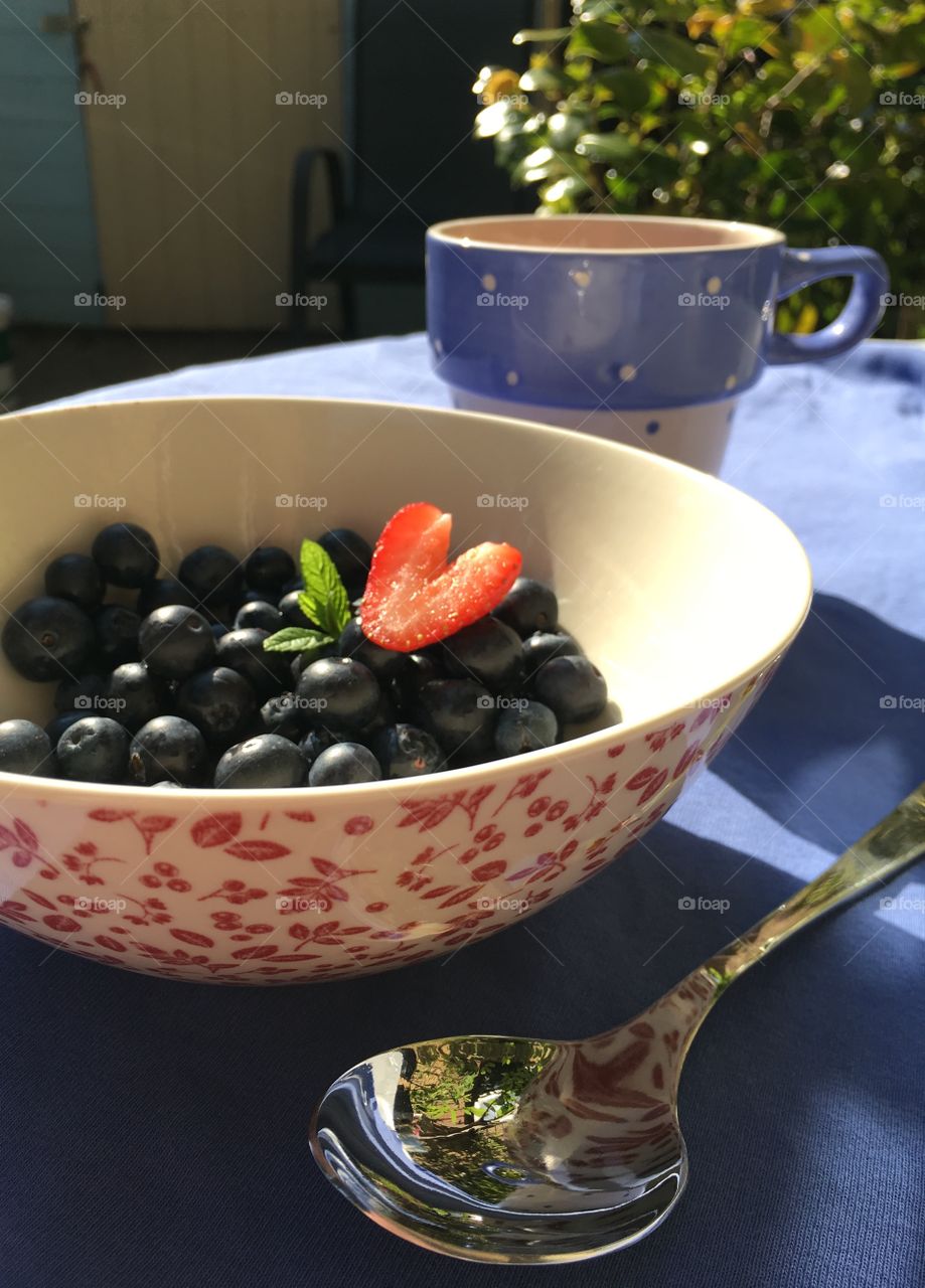Lovely bowl of blueberries with a strawberry heart and mint outside in the garden in summer