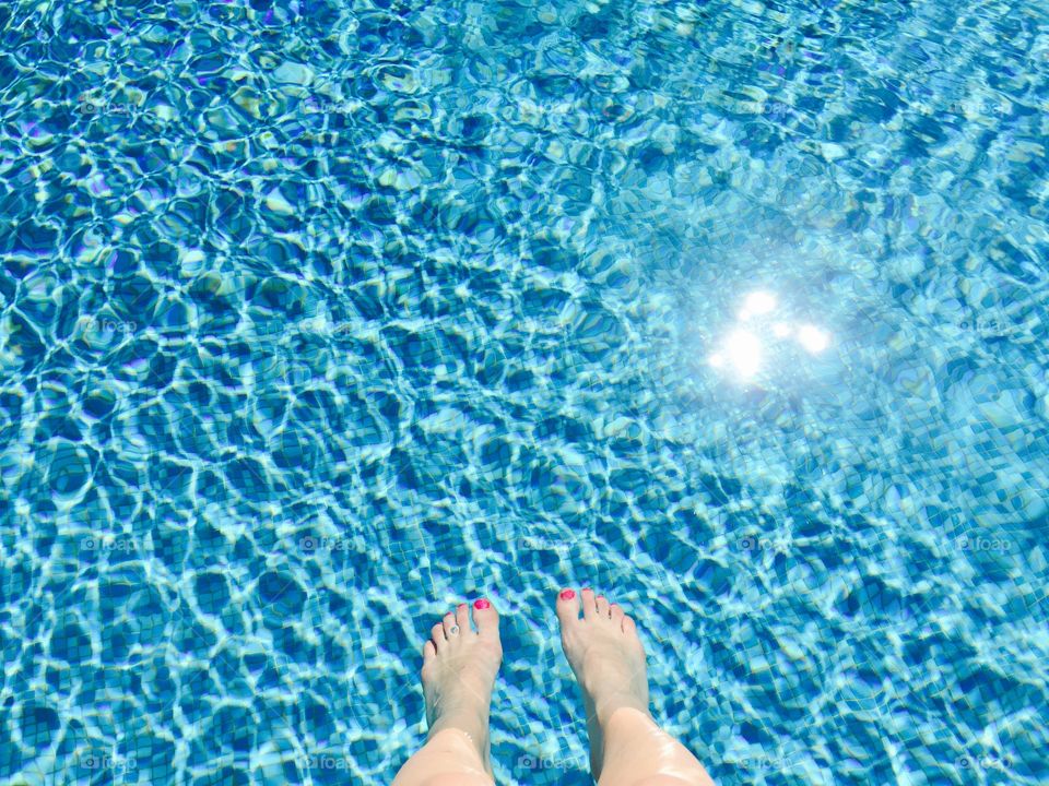 Woman's feet with red nailpolish in the pool