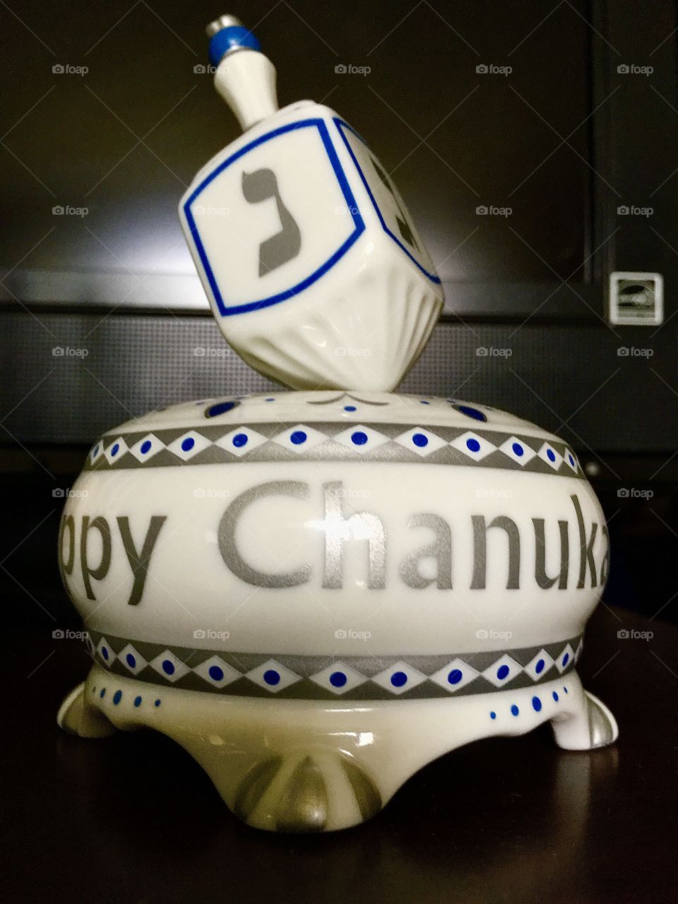 Chanukah decor in the form of an ornamental display piece, a porcelain dish, handcrafted with "Happy Chanukah" text painted across the base and a decorative dreidel on top, in the traditional blue and white colors.