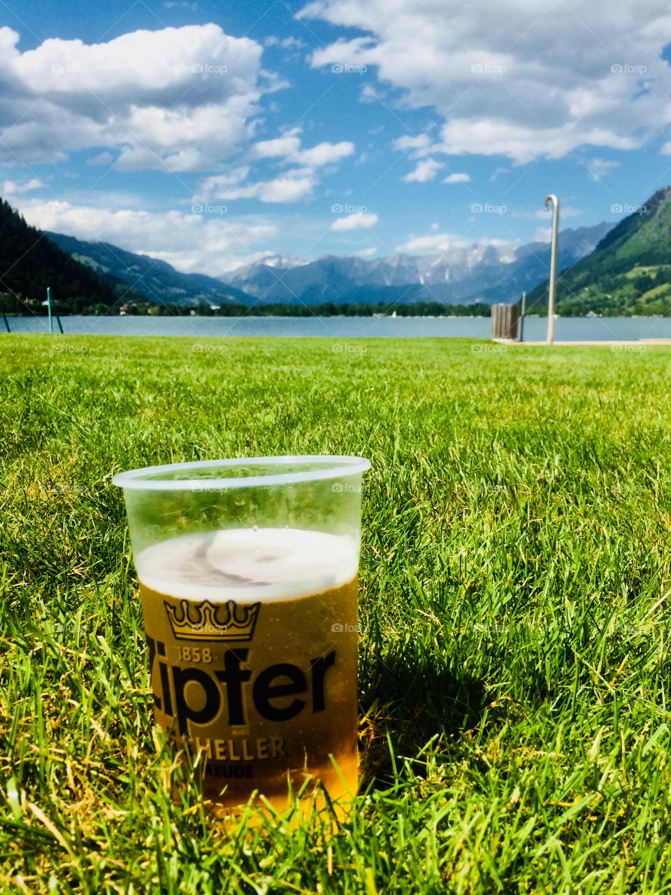 A glass of beer on a sunny day in grass with a view to lake and mountains