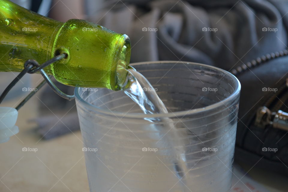 Water from green bottle decanter pouring into clear drinking glass