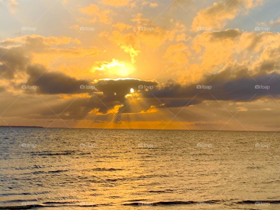 Sunset Rodeo - A spray of sunset rays escape from a cluster of dark clouds to reflect on the waters surface