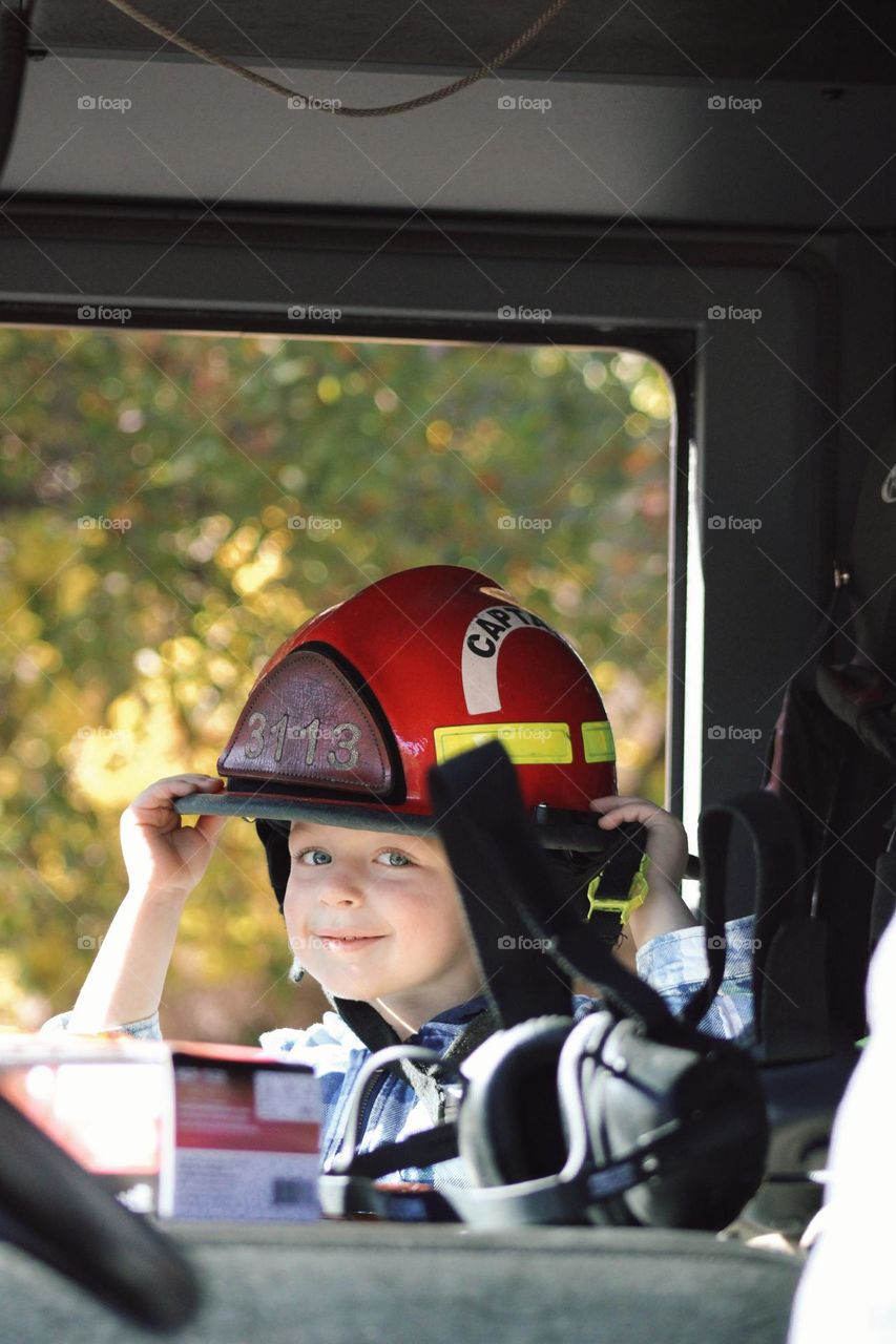 Little boy sitting in a fire truck wearing a Captains helmet 