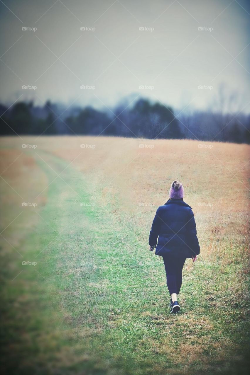 A warmly dressed female takes an evening stroll in a countryside clearing 