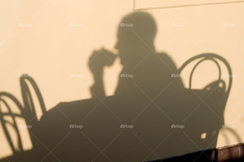 Soft, muted silhouette of a person drink coffee in the morning sun