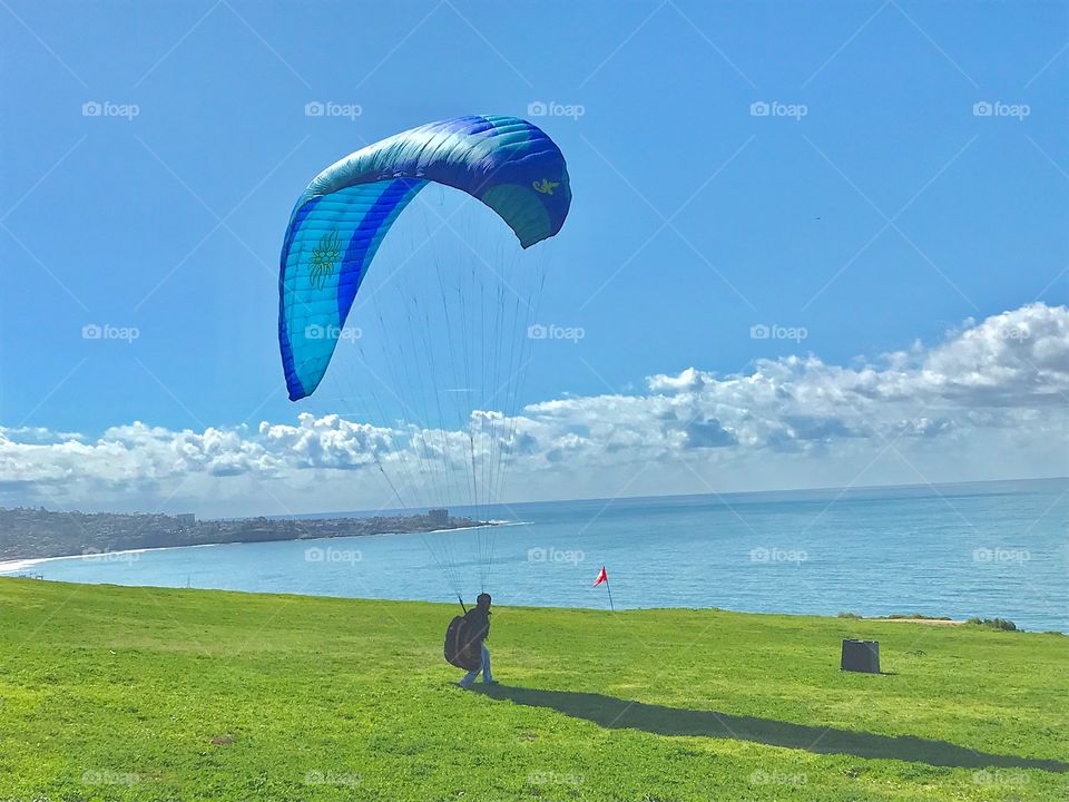 A person is practicing paragliding on top of a beautiful grassy coastal cliff in San Diego California. 
