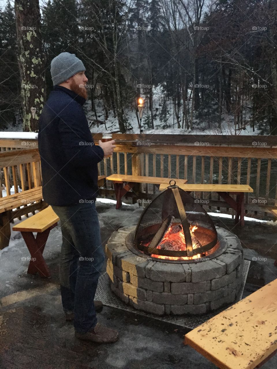 Young man standing near fire pit with drinking glass