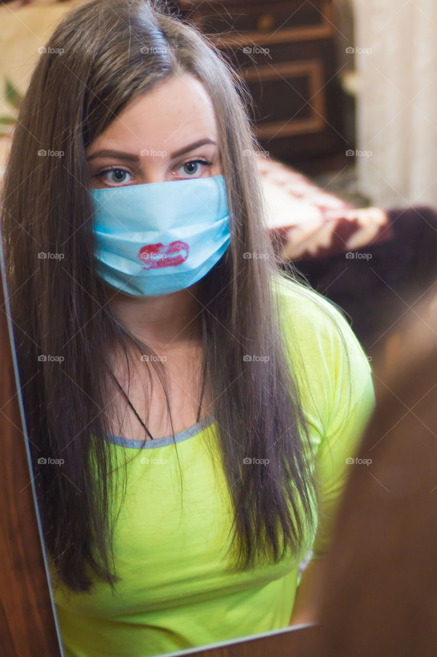 A young girl does makeup for a walk outside in a protective mask against the coronavirus pandemic, her lips are painted with red lipstick.