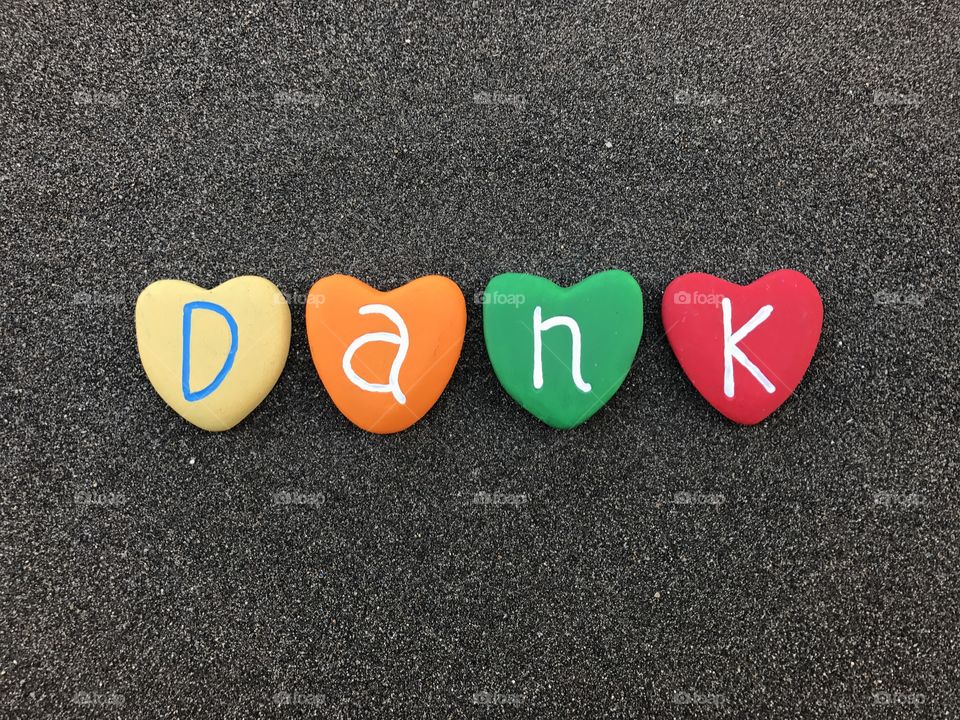 Dank, danish thank you with colored heart stones over  black volcanic sand