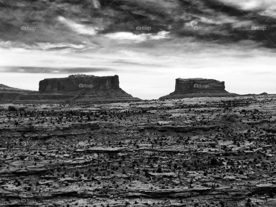Desert Mesa Black and White. The desert opens up as two mesa tower over them. 