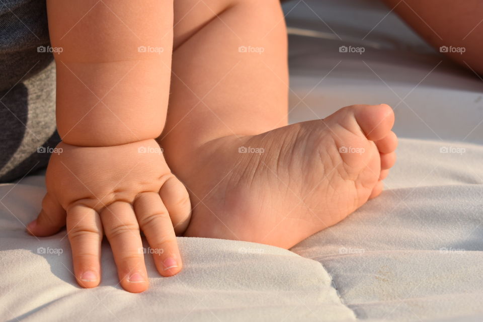 A close up of a baby’s chubby hand and foot, doused in gentle sunlight on a beige blanket. 