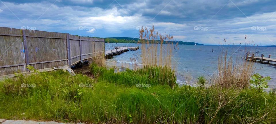 From behind the clouds the sun is beginning to peak through here at the shore of the “Starnberger See”, the large freshwater lake near the small town of “Starnberg” in rural “Bavaria”. 2023. Hypnotic Productions