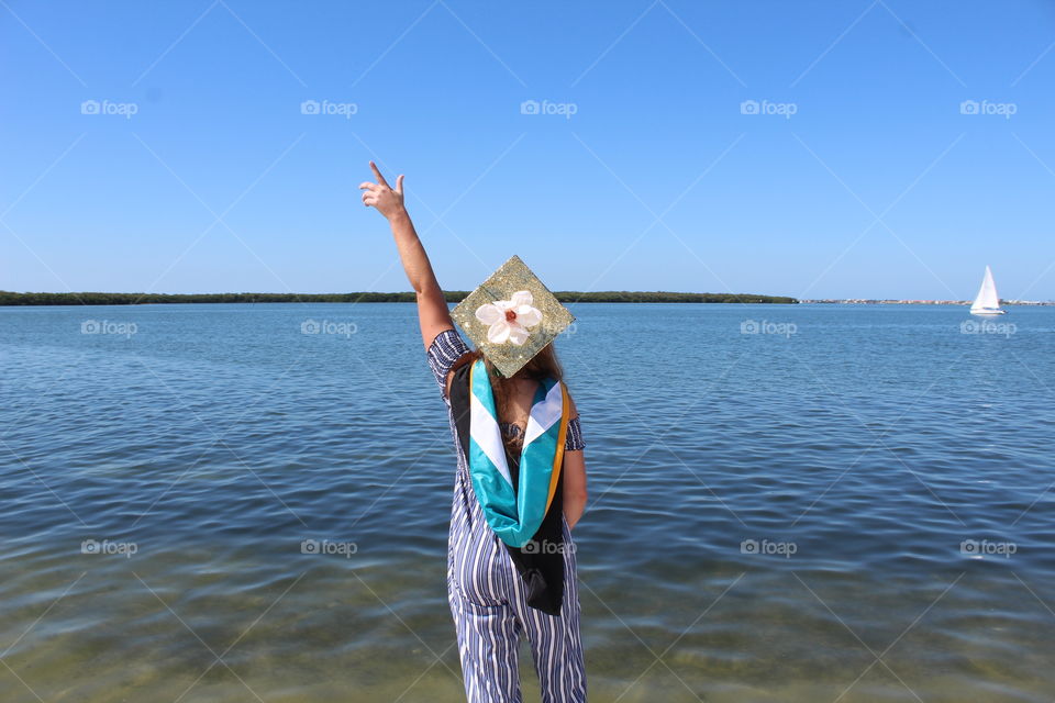 A girl celebrating college graduation over the ocean side.