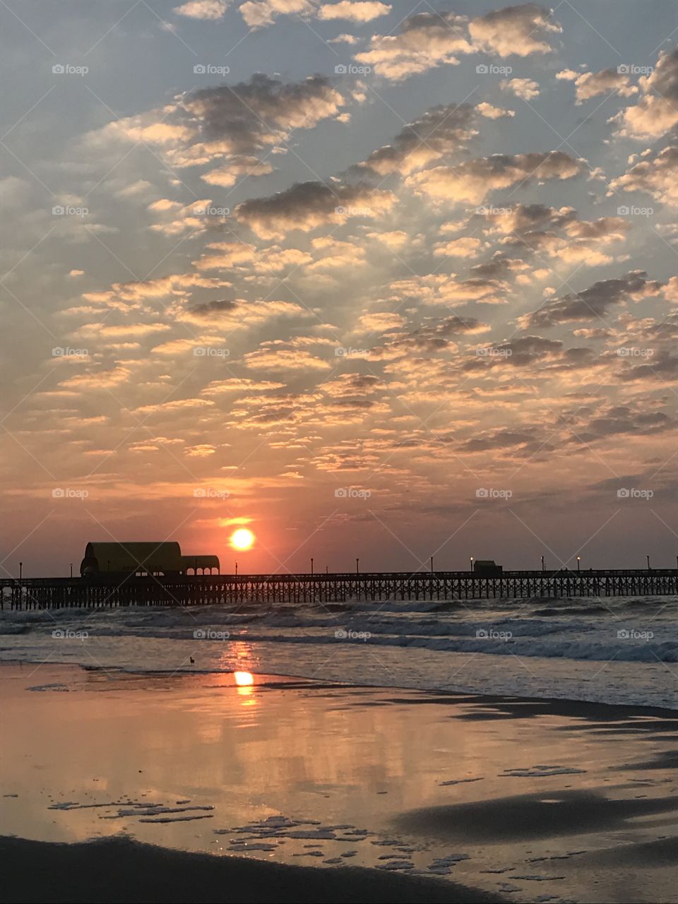 A beautiful, warm summer sunrise on the Myrtle Beach coast. A gorgeous salmon-colored sun shines and illuminates the cool waters.