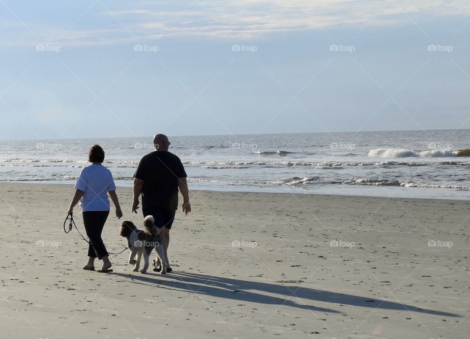 Husband and wife taking a morning walk with their dog on the beach