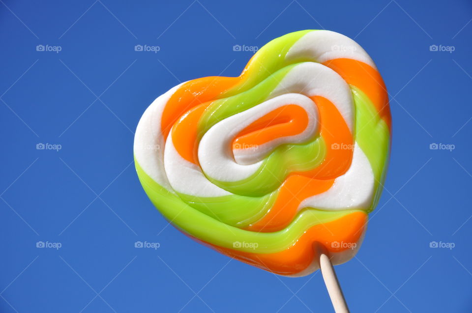 Foap mission Sugar: A heart shaped lollipop against a bright blue sky. 