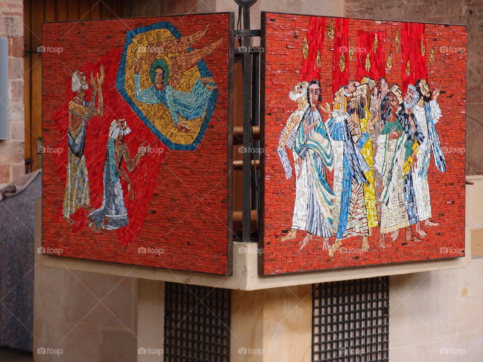 Wall hangings of religious scenes made from small and bright tiles in a European church. 