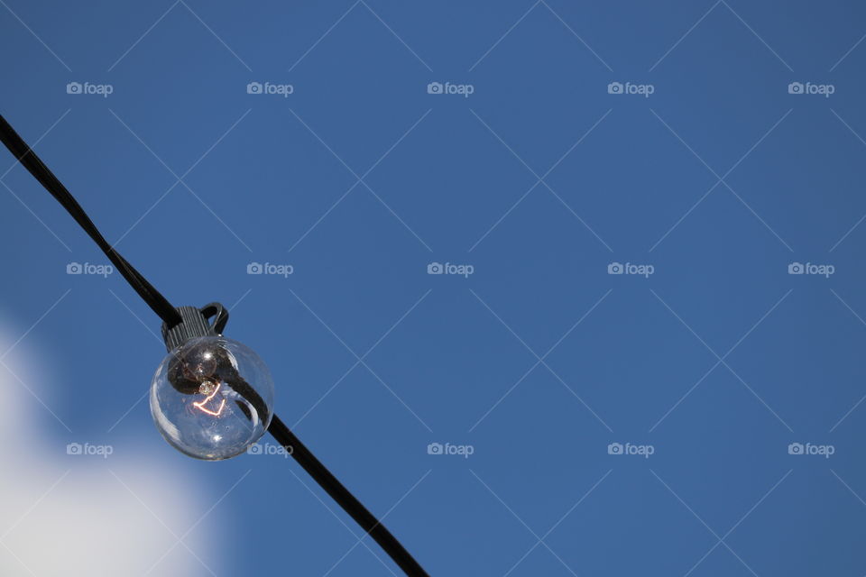 Lit Round lightbulb on a wire against a vivid clear blue sky daytime, minimalistic image with plenty of room for copy 