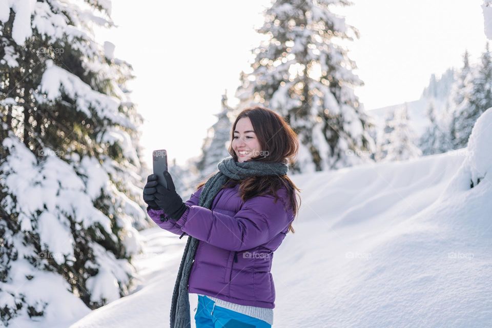 Young woman using her phone to speak on social media, while in nature doing a hike in winter.