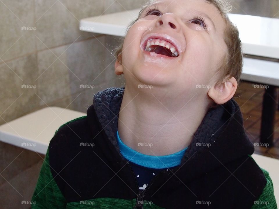 A little boy has a big laugh over the vanilla ice cream covering his mouth after eating a cone for dessert. 