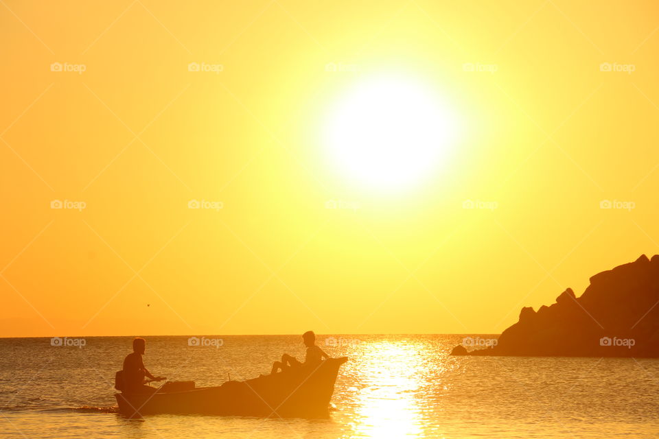 Silhouette of fisherman sitting on boat at sunset
