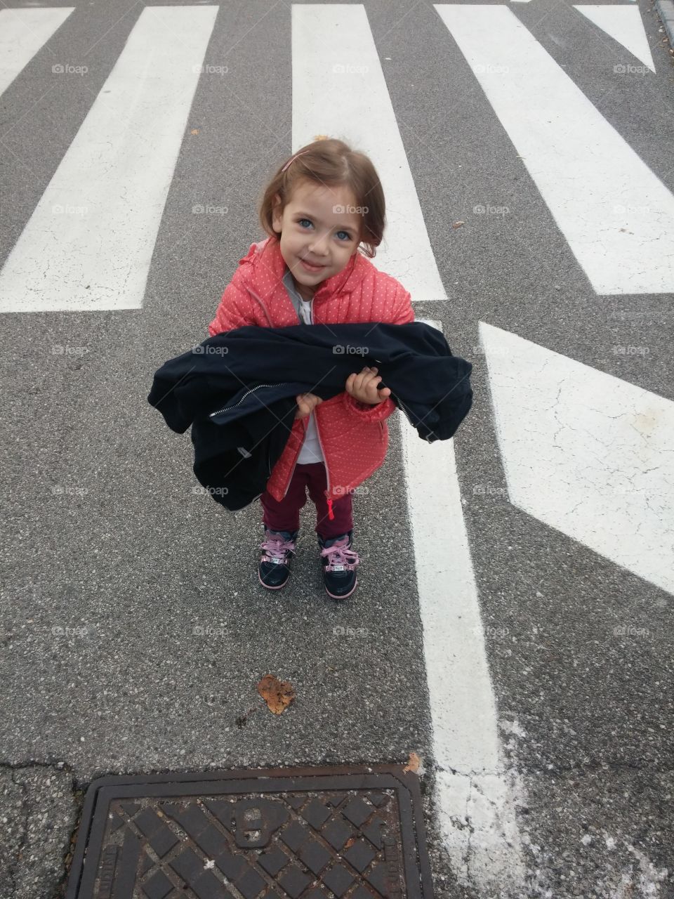 A little girl holding jacket standing on road