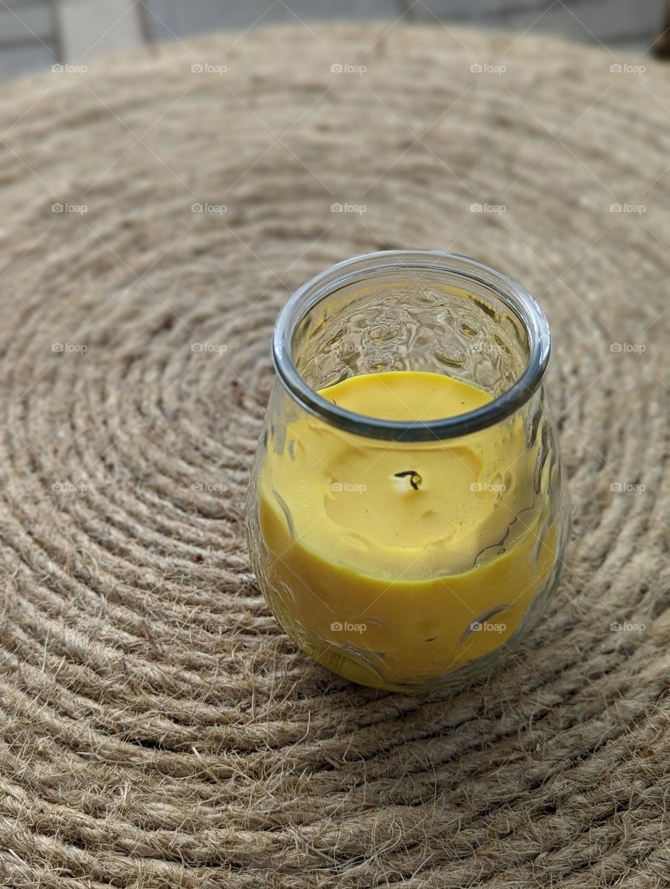 bright yellow citronella candle in glass jar on a rope ottoman outside patio vibes