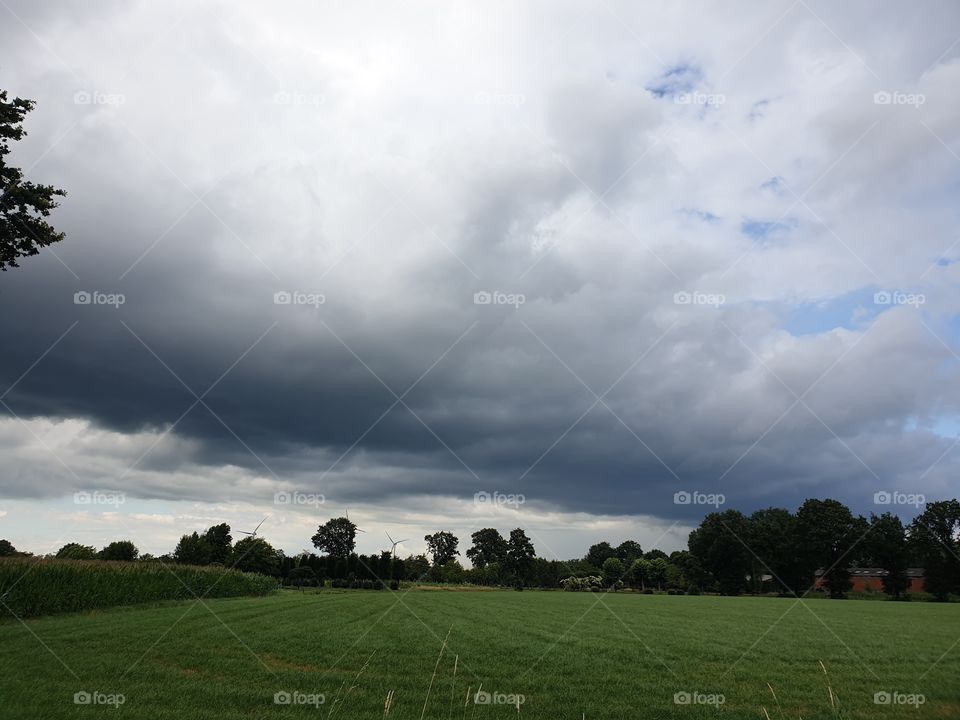 A landscape portrait of a storm cloud over a meadow grass field. the cloud looks very intimidating and dark.