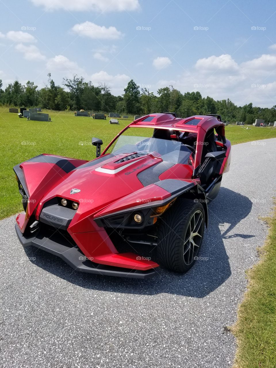 This is a modified polaris slingshot. its sitting at a church, in the back ground pretty green nature with trees.