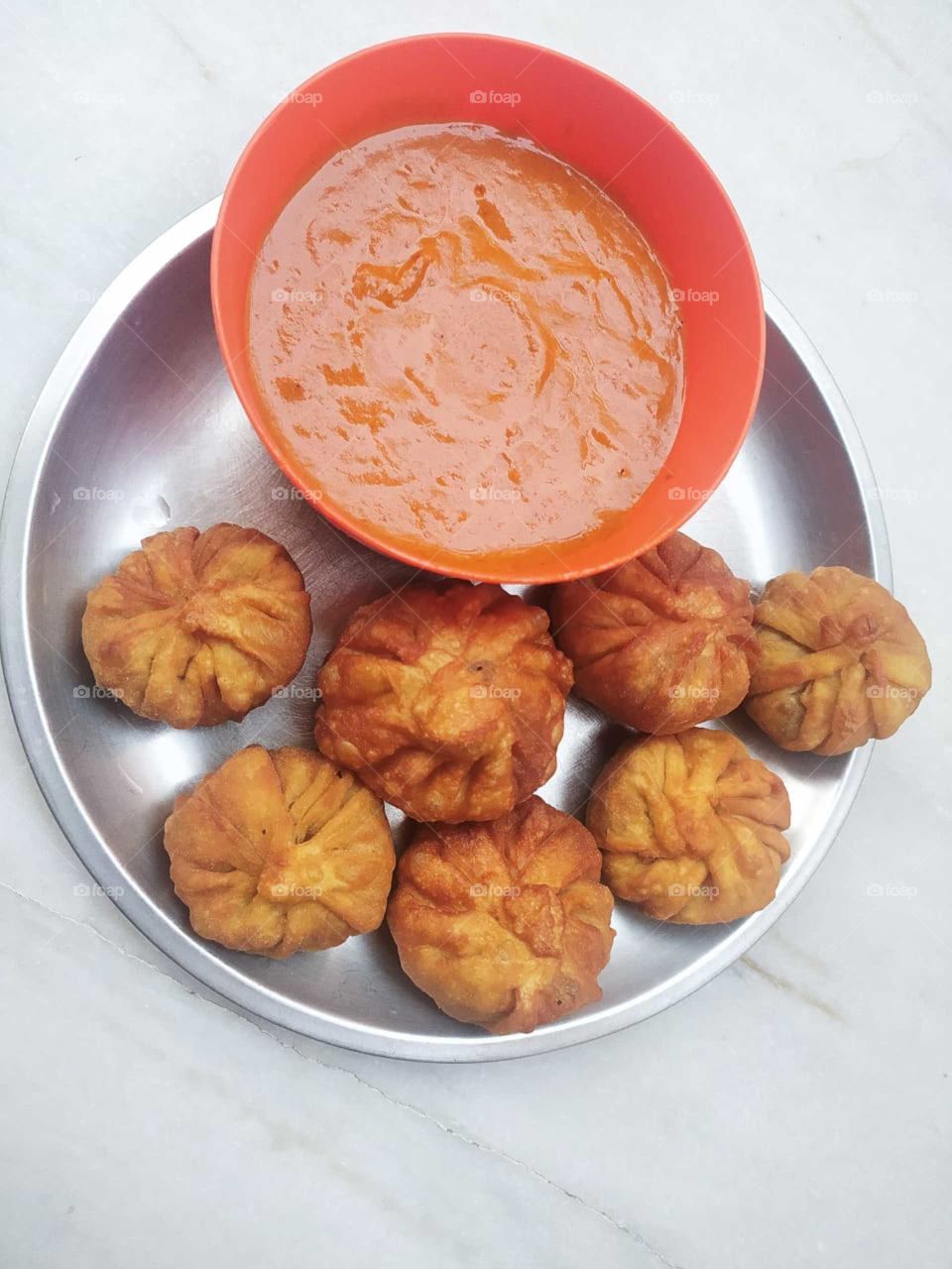 Veg Fried Momos are crispy & delicious deep-fried dumplings made of plain flour stuffed with crunchy & mildly spiced vegetables.
The name ‘momos’ is believed to be a colloquial form of the Tibetan word ‘mog mog’. Momos are considered native to Tibet.