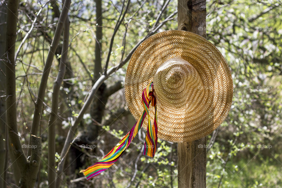 Straw summer hat hanging on wooden pole at the backyard, sunlight and wind