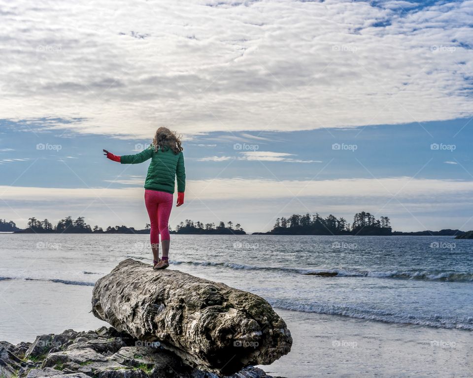 Girl balances on a huge driftwood log at the Pacific Ocean in Tofino, British Columbia, Canada 