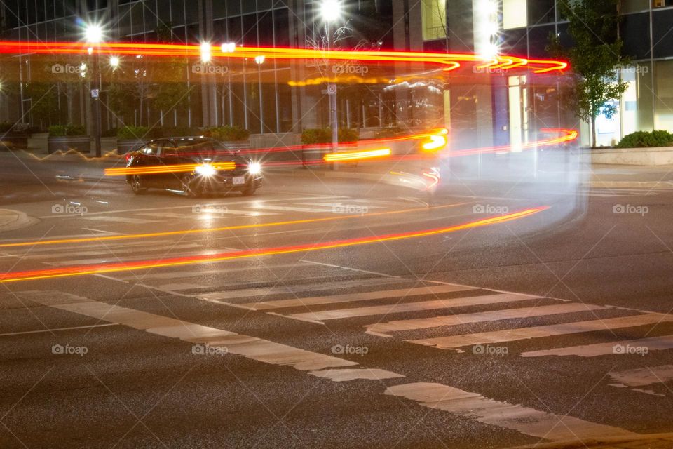 Long exposure of a white van as it turns the corner on a city street with a black car waiting to proceed.